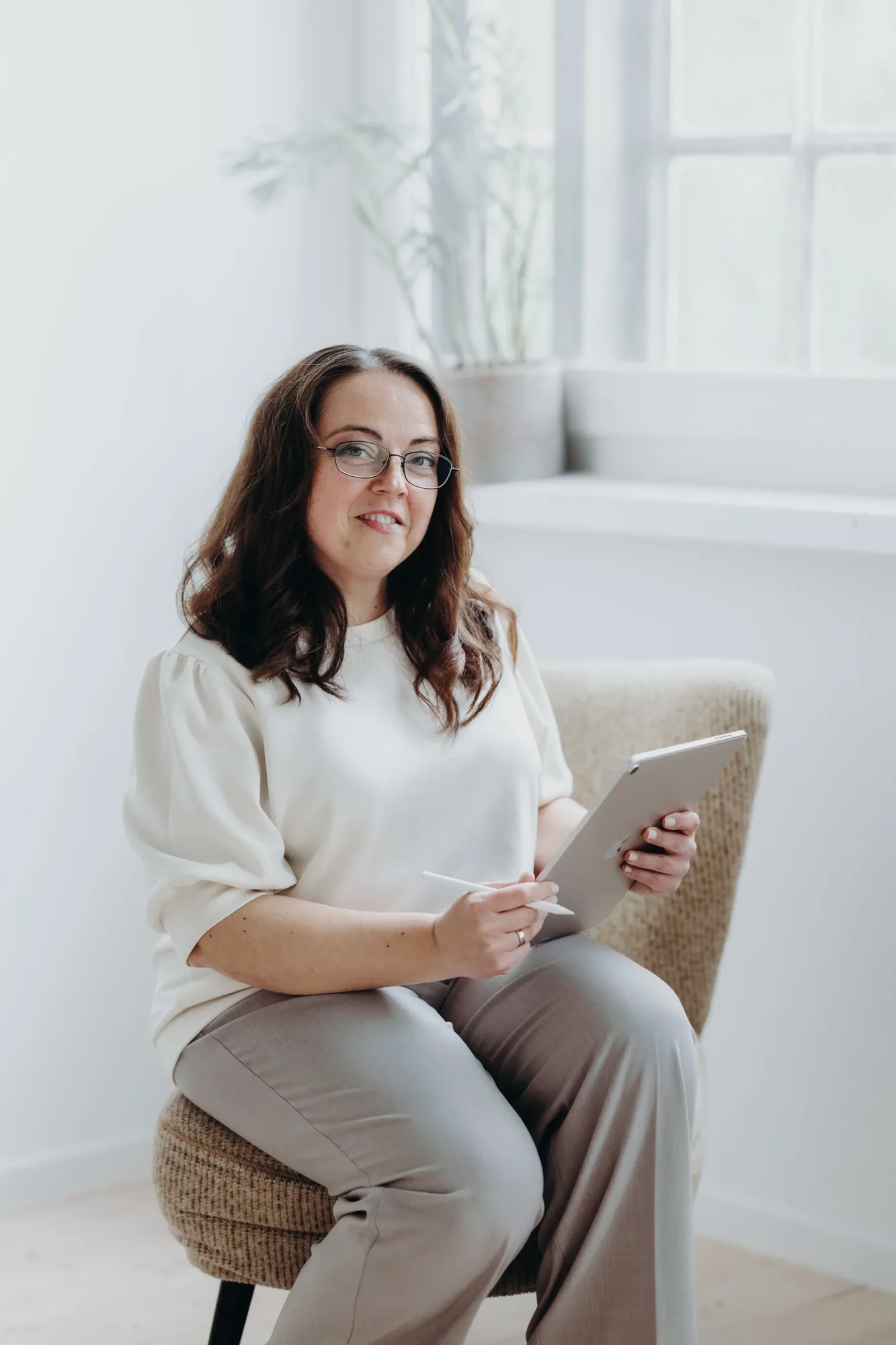 Marina Lübcke sitzt mit Tablet in einem Sessel und lächelt in die Kamera